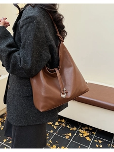 Detail of a brown leather tote bag with drawstring ties and silver ring on a model