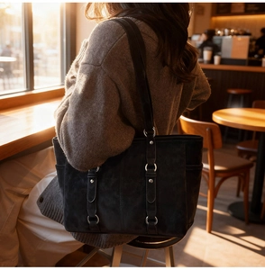 Detail view of a black suede tote bag with decorative straps and silver buckles in sunlight