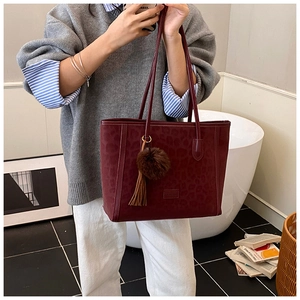 Close-up of deep red tote bag with leopard emboss, faux fur pompom and tassel detail