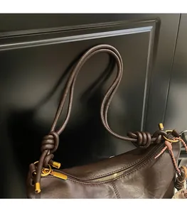 Detail of dark brown leather shoulder bag featuring knotted strap and gold hardware