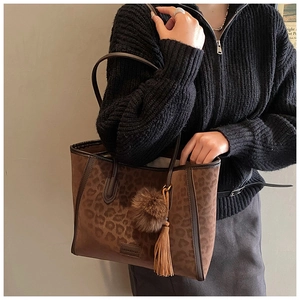 Detail of leopard print tote bag with soft suede texture, tassel charm, and logo stamp