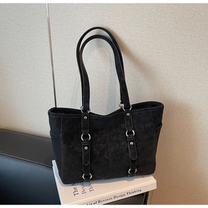 Detail of black suede tote bag with silver metal rings and rivets on white books