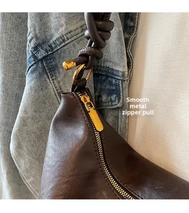 Detail of dark brown leather bag with golden zipper and knotted strap design