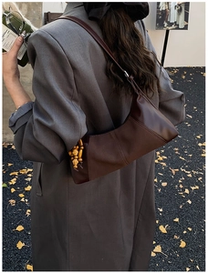 Détail du sac sous l'aisselle en cuir marron foncé avec pompon en perles de bois