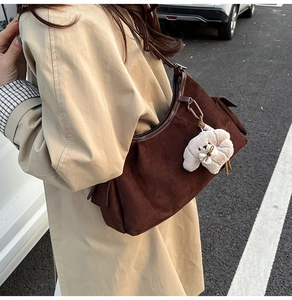 Détail d'un sac à main en daim marron foncé avec un pendentif chiot en peluche