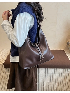 Detail of deep brown leather tote bag with metallic ring charm shown on a model