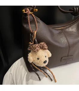 Macro detail of plush poodle charm with leopard bow on brown leather shoulder bag