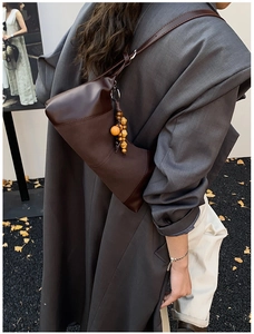 Détail d'un sac demi-lune en cuir marron foncé avec un pendentif vintage en perles de bois