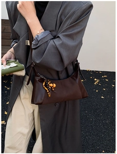 Détail du sac sous le bras en cuir marron foncé avec coutures et breloque en bois