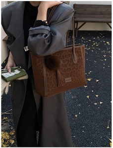 Close-up of leopard print tote bag with brown pompom and fringe detail in street style