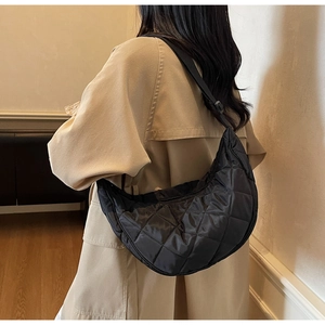 Dettaglio della borsa a mezzaluna nera trapuntata indossata su un trench beige