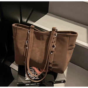 Detail of a brown suede tote bag with vertical stitching and side pockets in a studio setting