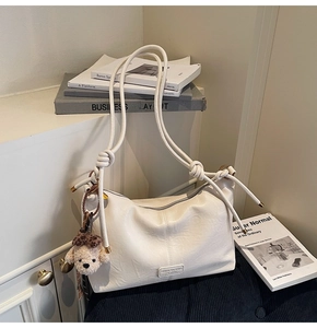 Detail of white textured leather crossbody bag featuring rope knot strap and plush bear charm