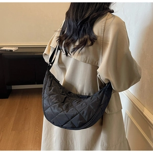 Back view of a model wearing a black quilted nylon half-moon bag over a beige coat
