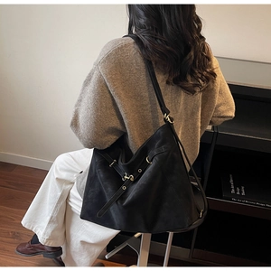 Detail of a large black vintage hobo bag with gold hardware worn by a model in a cozy room