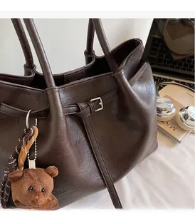 Detail of dark brown tote bag with high-shine leather texture and brown teddy bear charm