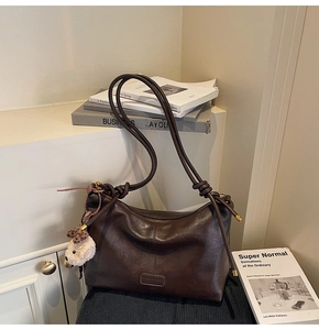 Detailed view of deep brown leather tote bag with vertical stitching and plush charm