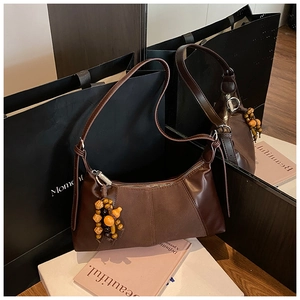 Détail du sac vintage marron foncé avec pompon en perles de bois et texture de cuir lisse