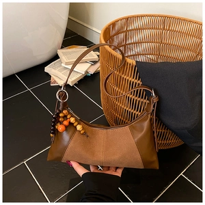 Détail du sac sous le bras marron vintage avec patchwork de daim et pompon en perles de bois