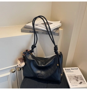 Detail of black PU leather tote with knot strap, leopard bear charm, and embossed logo