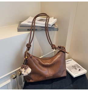 Detail of a brown leather tote bag featuring stylish knotted straps and a plush dog charm