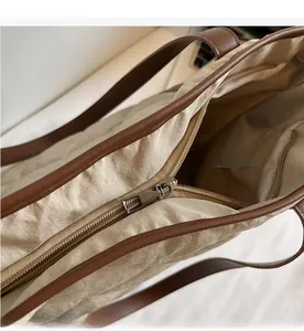 Close-up of beige wrinkled tote bag with smooth zipper closure and brown leather trim