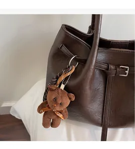 Detail of cute brown plush bear charm with bow on a vintage leather shoulder bag