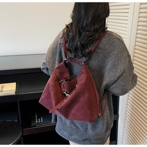 Detail of vintage burgundy suede shoulder bag with elegant gold-tone hardware on model