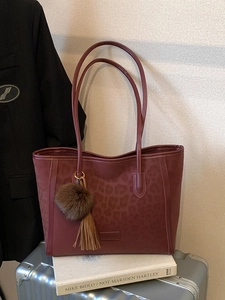 Burgundy leopard print tote bag with plush keychain on silver luggage background