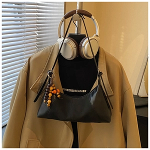Détail du sac hobo en cuir mat noir avec un charm en perles de bois sur la bandoulière