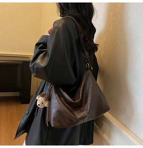 Detail of soft brown leather hobo bag with teddy bear charm and brand logo tag