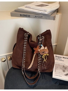 Sac fourre-tout marron en daim avec chaînes argentées et pendentif ours sur une chaise