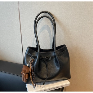 Detail of black faux leather tote bag with buckle and brown teddy bear plush charm