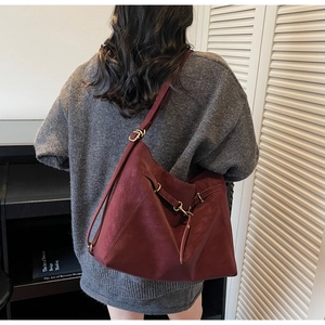 Detail view of burgundy leather shoulder bag with decorative strap and metal clasp on model