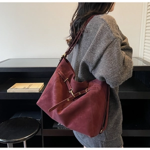 Detail of burgundy suede tote bag with metallic eyelets and gold buckle on a model