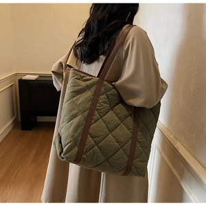 Olive green quilted tote bag with brown leather handles worn over a stylish trench coat