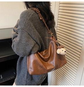 Detail view of brown leather hobo bag with thick knot strap and plush leopard charm
