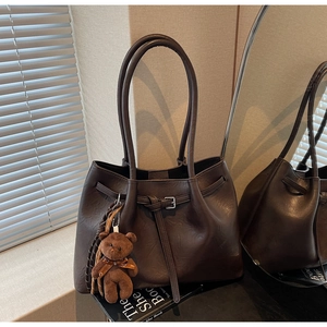 Detail of chocolate brown tote bag with decorative buckle and plush teddy bear charm