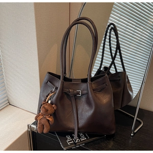 Detail of dark brown leather tote bag with vintage texture and cute bear pendant accessory