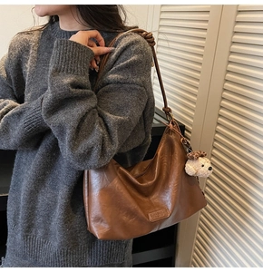 Detailed close-up of brown vintage crescent shoulder bag with knot strap and plush dog charm