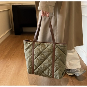 Close-up of olive green quilted tote bag featuring brown leather trim and handles