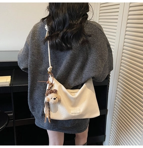 Detailed view of cream hobo tote bag worn on shoulder with a cute brown bear charm