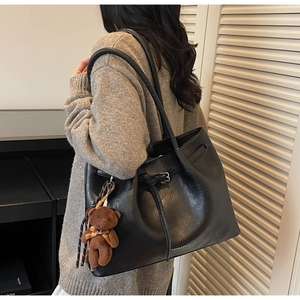 Detail of black faux leather tote bag with pleated texture and plush bear pendant