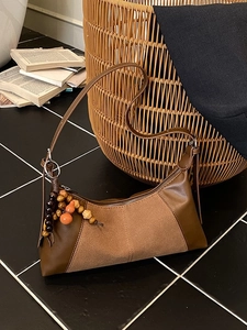 Sac baguette vintage marron avec pendentif perles posé sur un sol carrelé noir