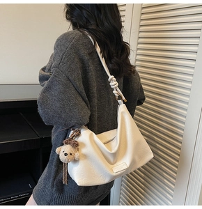 Detail of cream white leather tote bag with plush bear charm and knotted shoulder strap