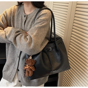 Close-up of black retro pleated leather tote with silver buckle and plush bear charm