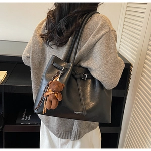 Detail of black leather tote bag featuring a plush bear pendant and logo print
