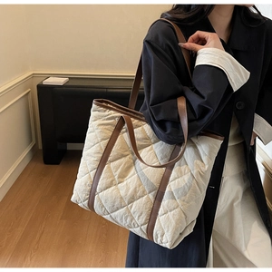 Detail shot of quilted texture and brown leather strap on cream tote bag