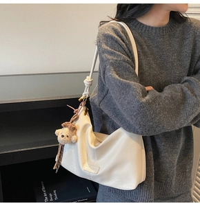 Detail of a creamy white soft leather hobo bag with a plush bear charm and knotted strap