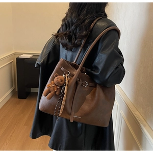 Detail of a brown pleated tote bag with a plush bear charm on a model in leather jacket